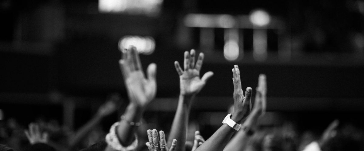 A group of people raising hands in a black and white concert setting, showing unity and celebration.